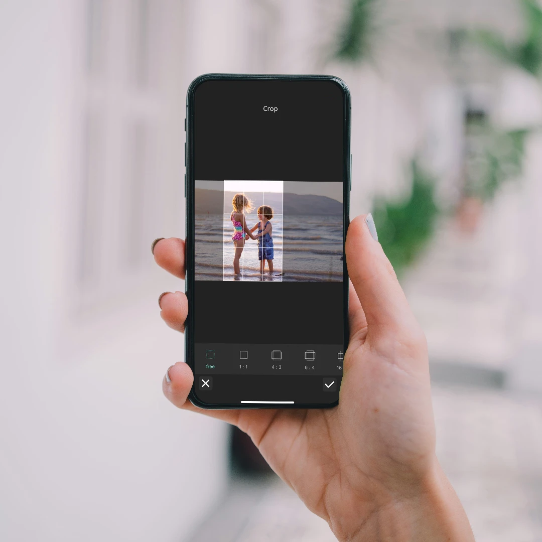 Hand holding smartphone with image of two children on beach being edited.