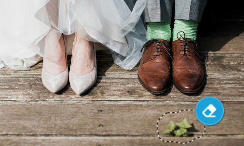 A bride's and groom's feet in wedding attire with mismatched socks on wooden floor.