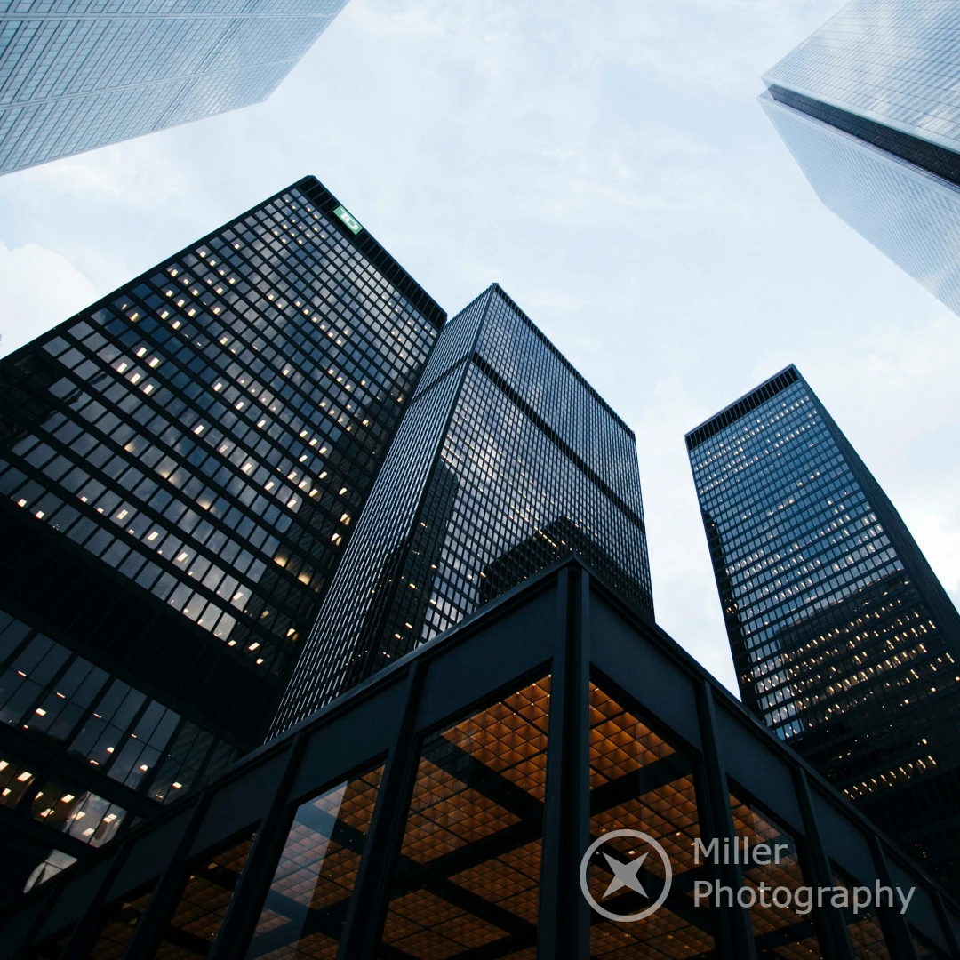 Low-angle view of modern skyscrapers with glass façades against a cloudy sky, showcasing urban architecture and reflections.